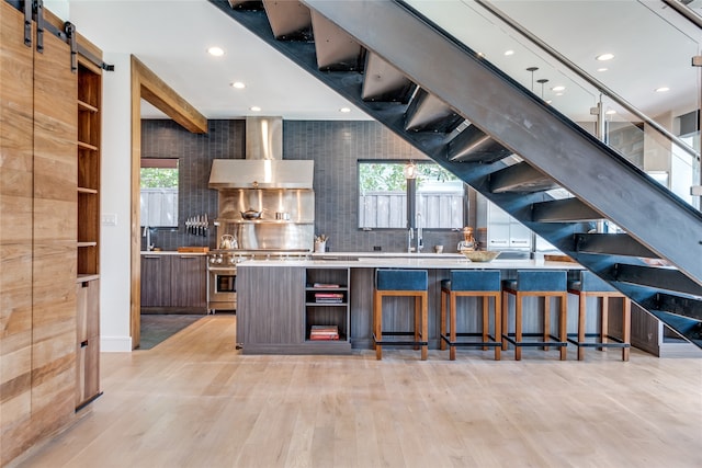 kitchen featuring wall chimney range hood, backsplash, a barn door, and plenty of natural light