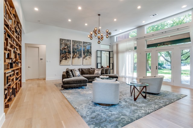 living room with a towering ceiling, a notable chandelier, and light hardwood / wood-style flooring