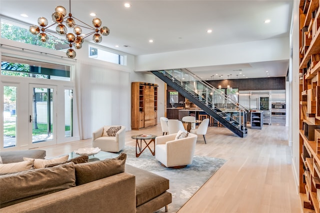 living room featuring a towering ceiling, a wealth of natural light, an inviting chandelier, and light hardwood / wood-style floors