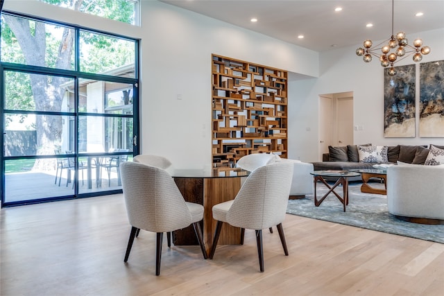 dining space featuring light wood-type flooring, a towering ceiling, and an inviting chandelier