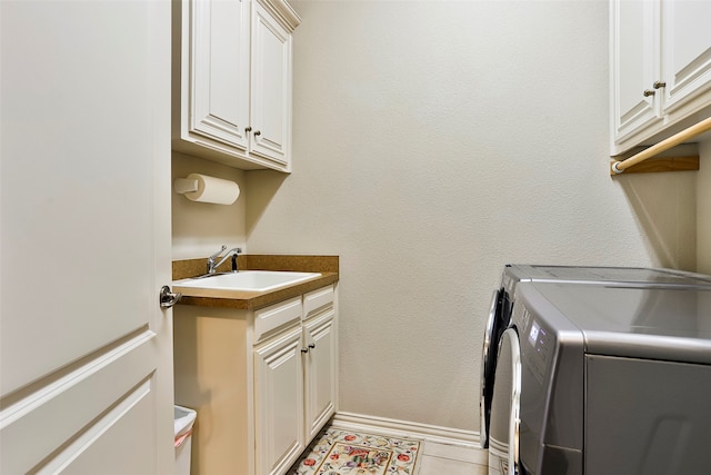 clothes washing area with light tile patterned floors, washing machine and clothes dryer, cabinets, and sink