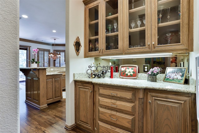 bar featuring light stone counters, dark hardwood / wood-style floors, a notable chandelier, and ornamental molding