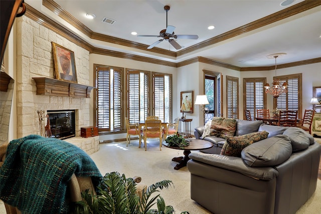 living room with crown molding, ceiling fan with notable chandelier, a stone fireplace, and carpet floors