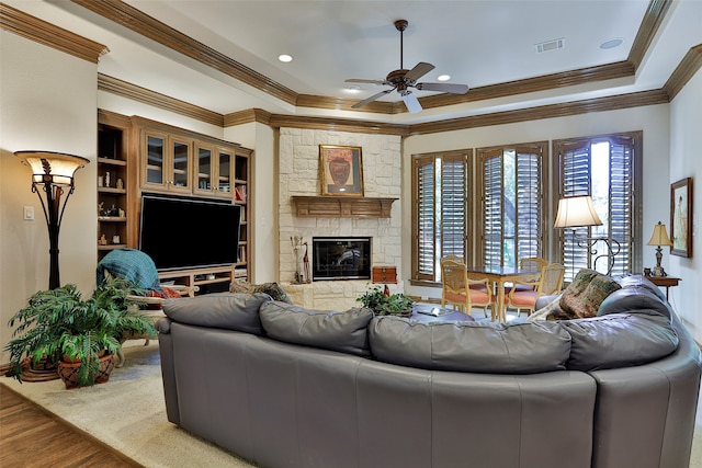 living room featuring ornamental molding, wood-type flooring, ceiling fan, and a stone fireplace