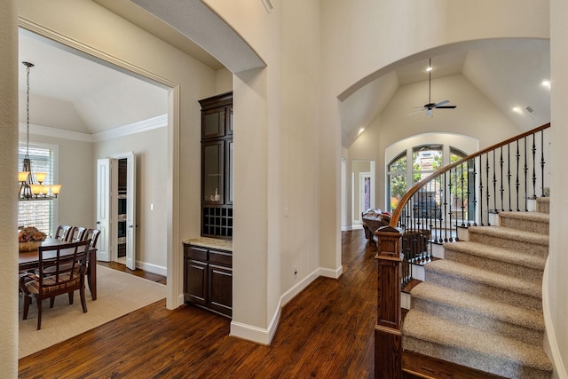 foyer entrance featuring ceiling fan with notable chandelier, ornamental molding, vaulted ceiling, and dark hardwood / wood-style floors