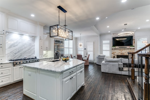 kitchen featuring a center island with sink, dark hardwood / wood-style flooring, white cabinetry, pendant lighting, and light stone counters