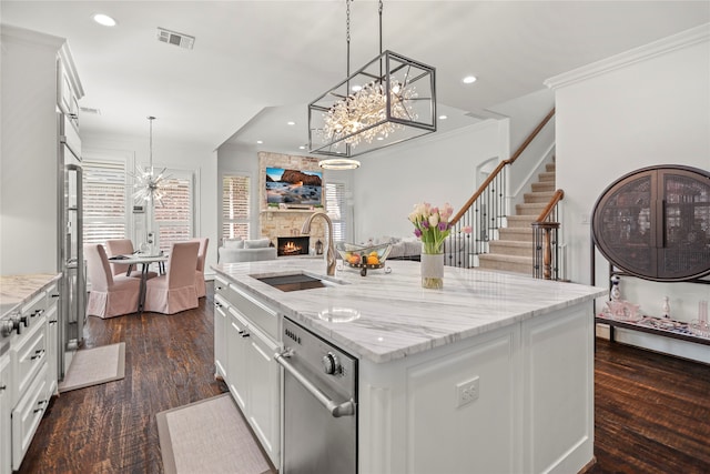 kitchen featuring white cabinets, a kitchen island with sink, dark hardwood / wood-style floors, a fireplace, and decorative light fixtures