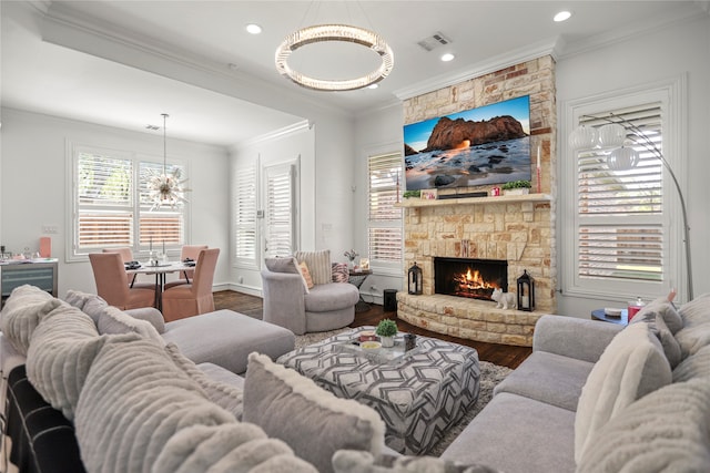 living room with hardwood / wood-style flooring, ornamental molding, an inviting chandelier, and a stone fireplace