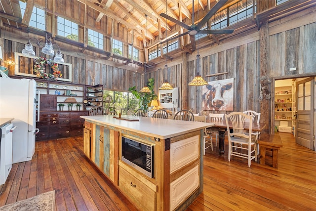 kitchen with stainless steel microwave, high vaulted ceiling, dark wood-type flooring, and pendant lighting