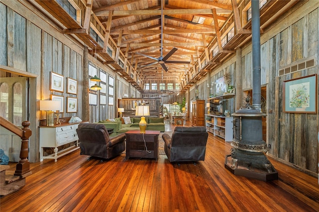 living room with a wood stove, high vaulted ceiling, hardwood / wood-style flooring, ceiling fan, and wooden walls