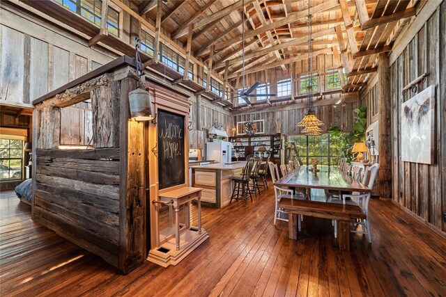 dining area with high vaulted ceiling, a wealth of natural light, wooden walls, and dark hardwood / wood-style floors