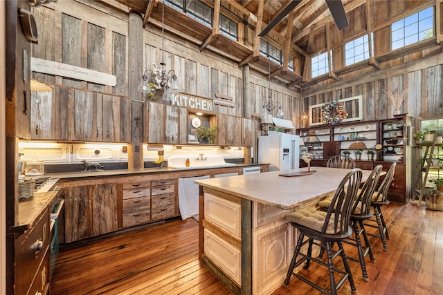 kitchen featuring wooden walls, white refrigerator with ice dispenser, dishwashing machine, a towering ceiling, and dark wood-type flooring