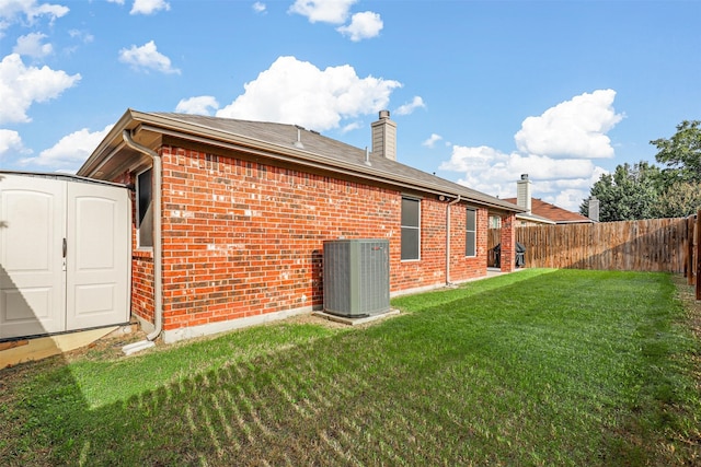 back of property with a storage shed, a lawn, and central air condition unit