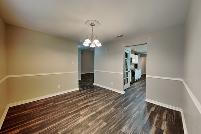 empty room with dark wood-type flooring and an inviting chandelier