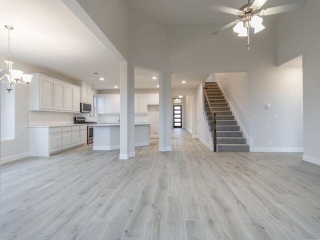 unfurnished living room featuring ceiling fan with notable chandelier, light wood-type flooring, and a towering ceiling