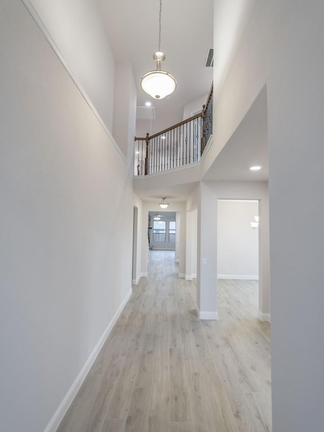 hallway with a towering ceiling and light hardwood / wood-style flooring