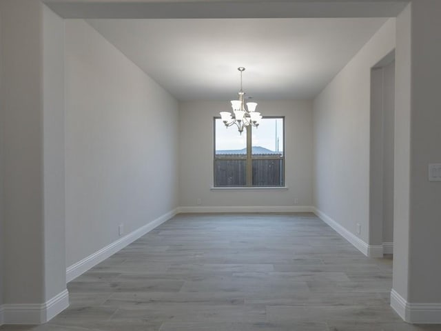 unfurnished room featuring an inviting chandelier and light hardwood / wood-style flooring