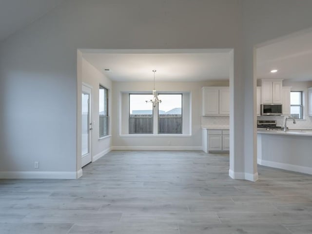 unfurnished living room with sink, a notable chandelier, and light wood-type flooring