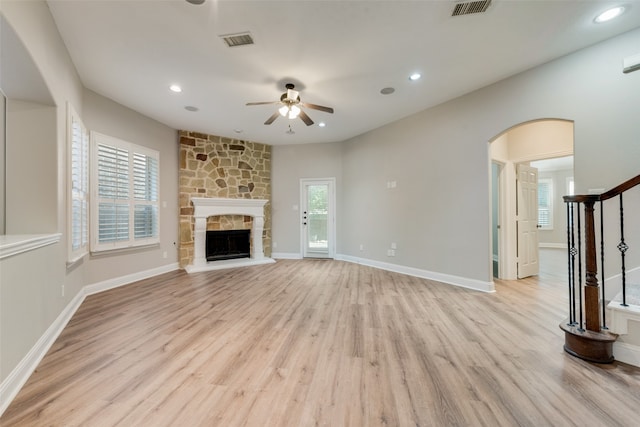 unfurnished living room with light wood-type flooring, ceiling fan, and a stone fireplace