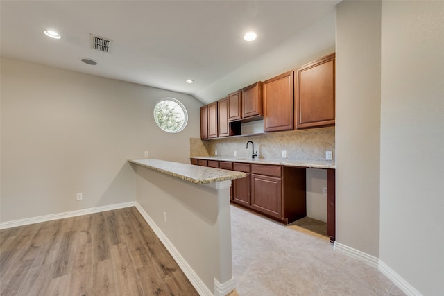 kitchen with vaulted ceiling, light hardwood / wood-style flooring, tasteful backsplash, kitchen peninsula, and sink