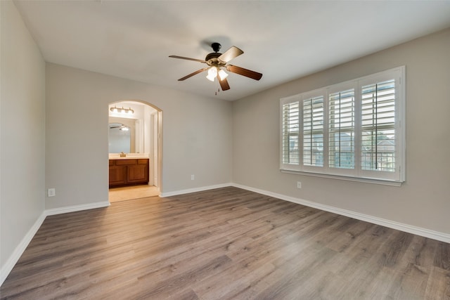 unfurnished bedroom featuring ceiling fan, connected bathroom, wood-type flooring, and sink