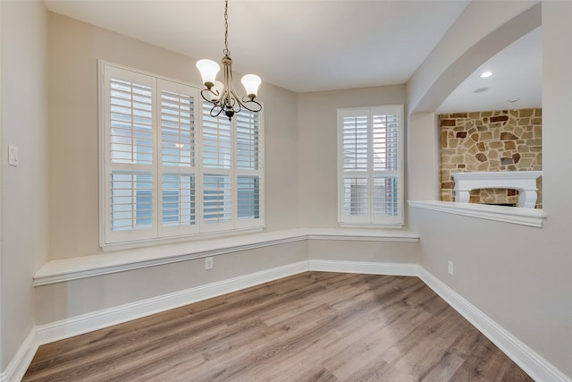 unfurnished dining area with hardwood / wood-style floors, a fireplace, and a notable chandelier