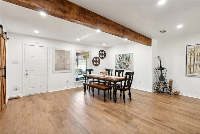 dining room featuring beam ceiling, a barn door, and light hardwood / wood-style floors