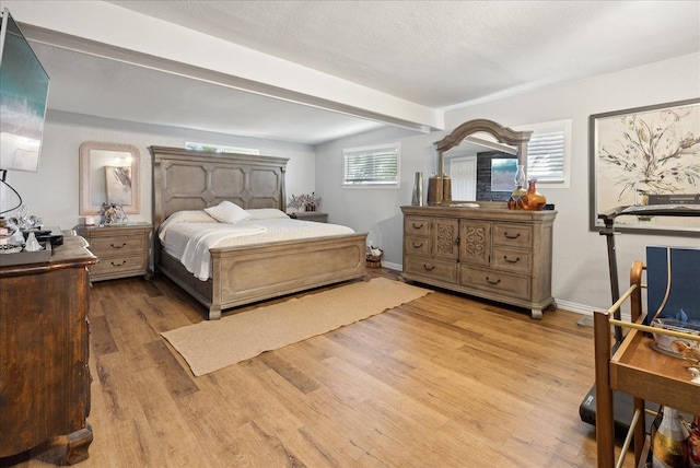 bedroom with light wood-type flooring, beamed ceiling, and a textured ceiling