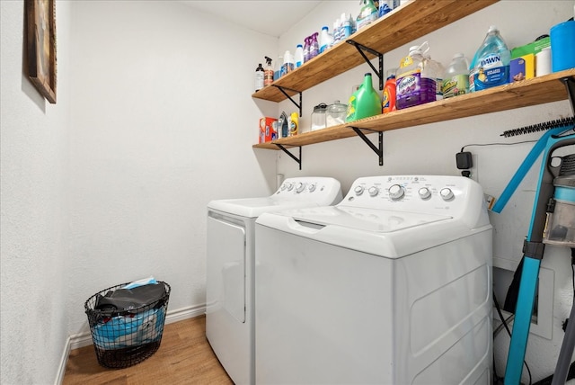 clothes washing area with washing machine and clothes dryer and light wood-type flooring