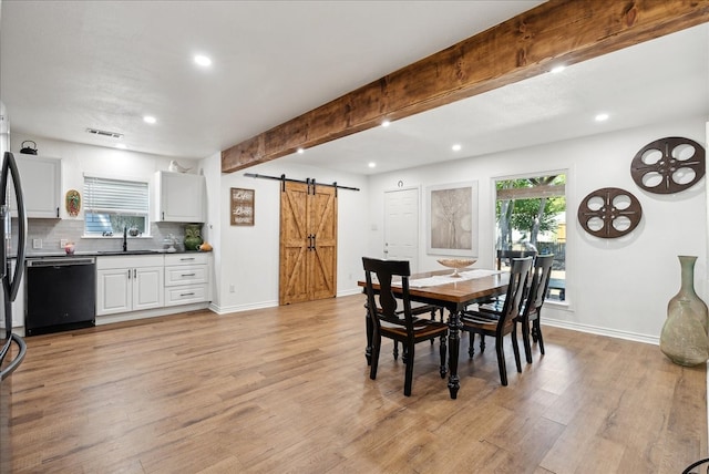 dining room featuring light wood-type flooring, plenty of natural light, beam ceiling, and a barn door