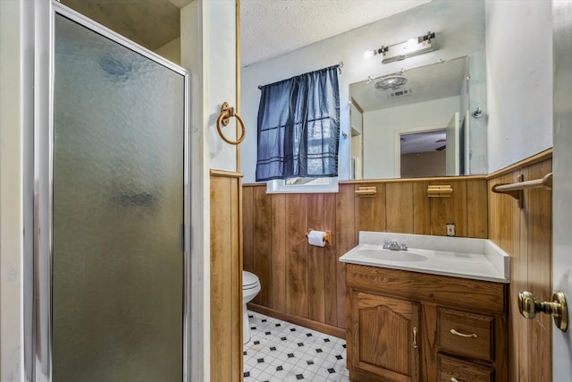 bathroom with a textured ceiling, vanity, wood walls, walk in shower, and toilet