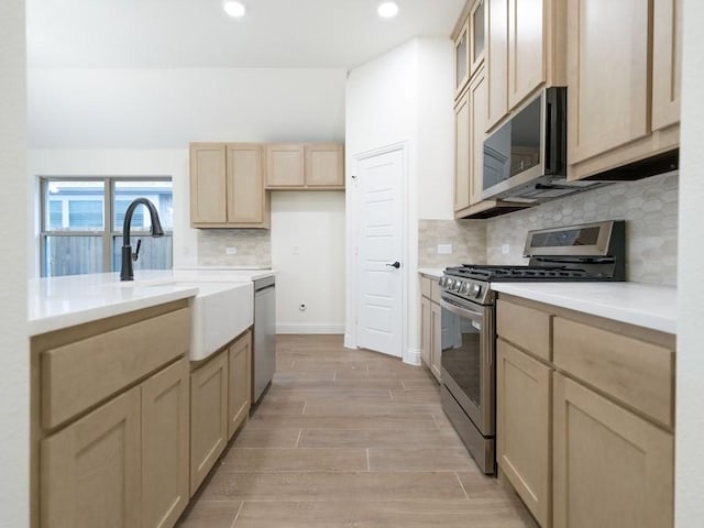 kitchen with decorative backsplash, light brown cabinetry, light wood-type flooring, stainless steel appliances, and sink