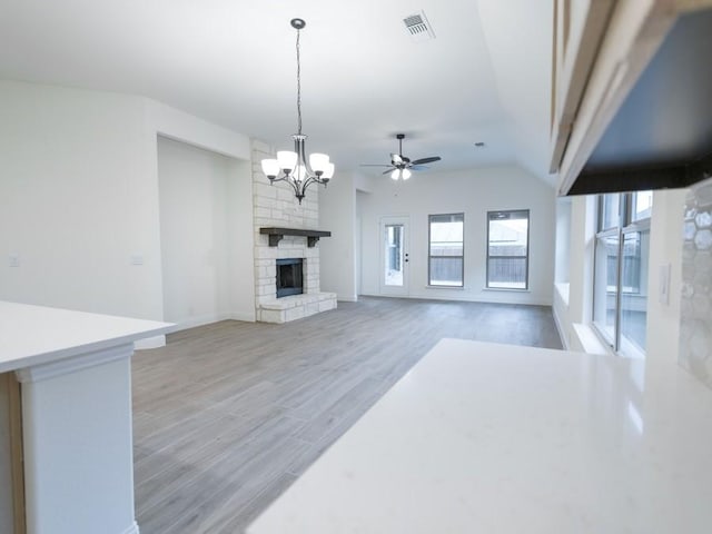 unfurnished living room with ceiling fan with notable chandelier, hardwood / wood-style flooring, a stone fireplace, and lofted ceiling