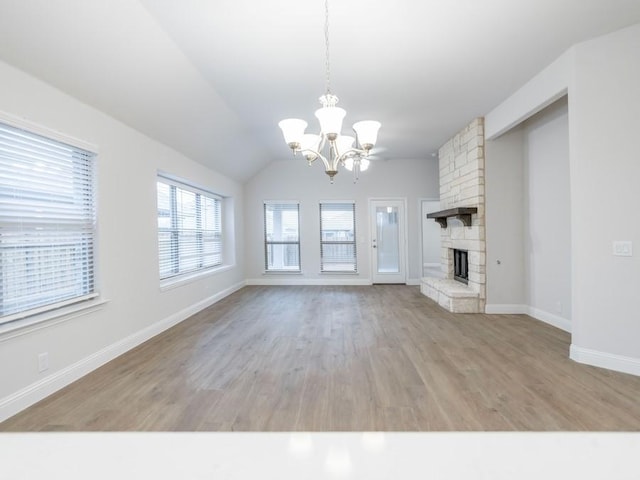 unfurnished living room with a chandelier, light hardwood / wood-style floors, a stone fireplace, and lofted ceiling