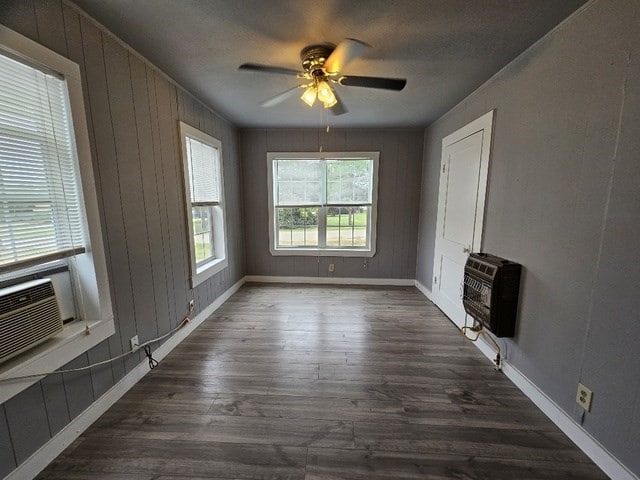 unfurnished living room featuring dark hardwood / wood-style floors, ceiling fan, wooden walls, and heating unit