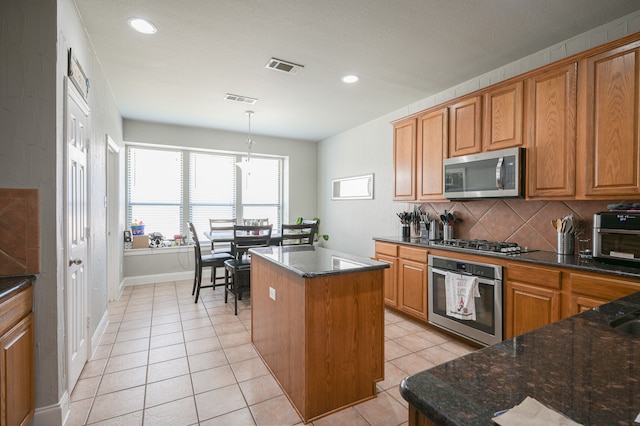 kitchen with pendant lighting, light tile patterned floors, a center island, stainless steel appliances, and dark stone countertops