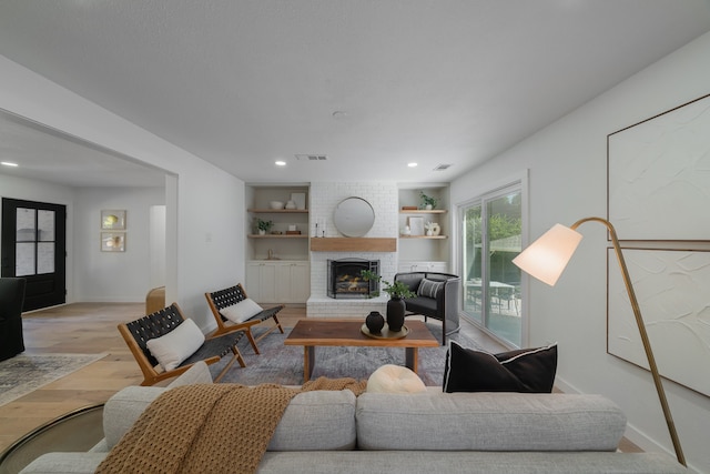 living room with a brick fireplace, light hardwood / wood-style flooring, and built in shelves