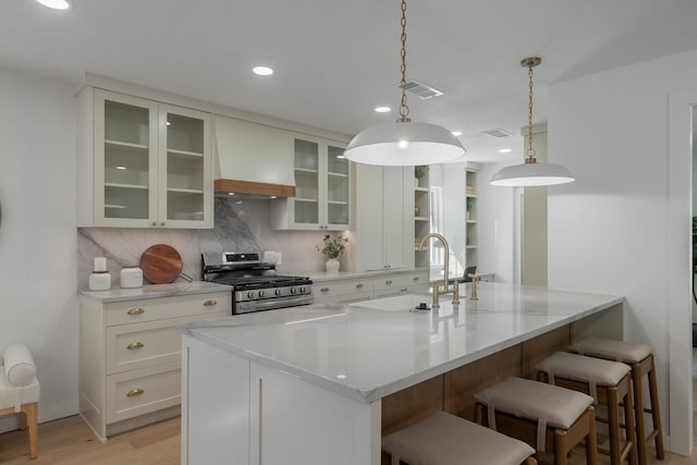 kitchen featuring hanging light fixtures, decorative backsplash, white cabinetry, sink, and stainless steel range with gas cooktop