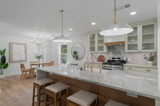 kitchen featuring hanging light fixtures, light stone countertops, light hardwood / wood-style floors, sink, and stainless steel range