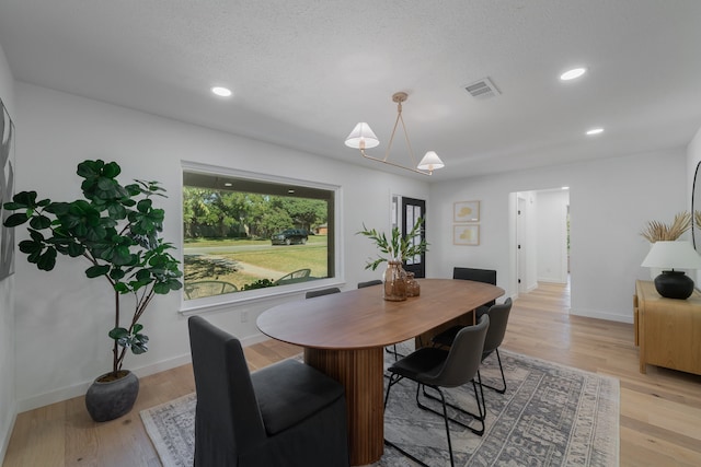 dining area with a textured ceiling, light wood-type flooring, and a chandelier