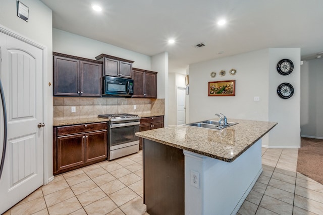 kitchen with stainless steel gas range, dark brown cabinets, sink, light tile patterned floors, and a center island with sink