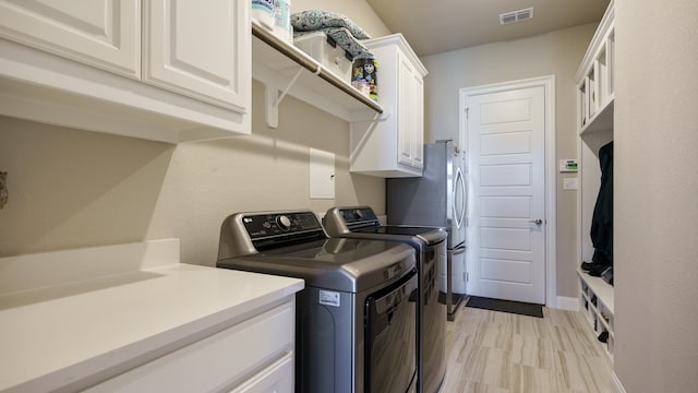 laundry room featuring cabinets, washer and clothes dryer, and light wood-type flooring