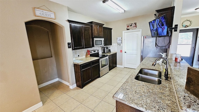 kitchen featuring sink, decorative backsplash, light stone countertops, appliances with stainless steel finishes, and dark brown cabinetry