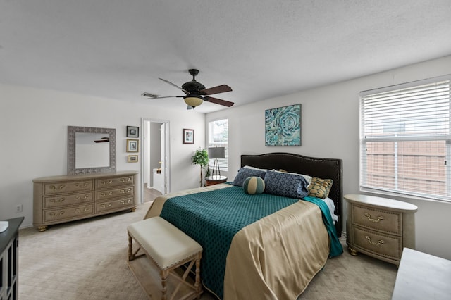 carpeted bedroom with a textured ceiling, ensuite bath, and ceiling fan