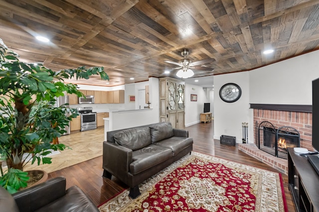 living room with a brick fireplace, ceiling fan, wood ceiling, and light wood-type flooring