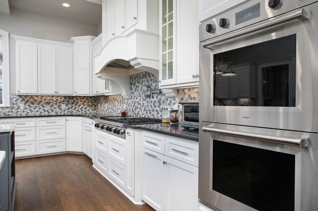 kitchen with white cabinets, backsplash, a fireplace, dark hardwood / wood-style flooring, and stainless steel appliances