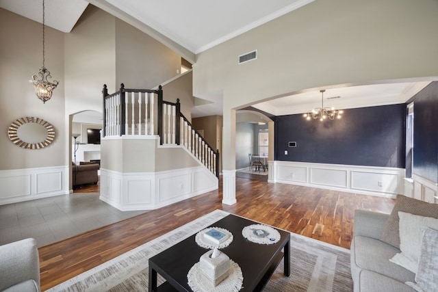 unfurnished living room with ornamental molding, a towering ceiling, wood-type flooring, and an inviting chandelier