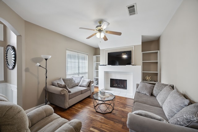 living room featuring built in shelves, ceiling fan, a tile fireplace, and dark hardwood / wood-style flooring