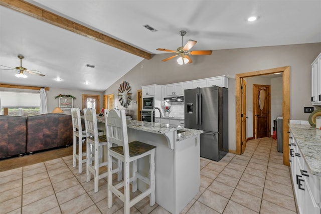 kitchen with white cabinets, a center island with sink, appliances with stainless steel finishes, a kitchen bar, and vaulted ceiling with beams