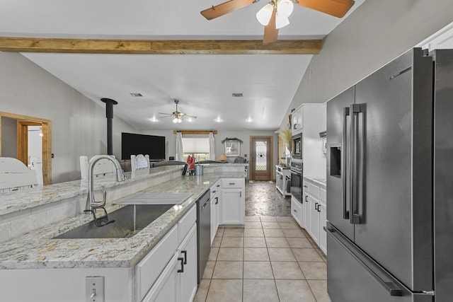 kitchen with sink, a wood stove, white cabinetry, stainless steel appliances, and light tile patterned floors